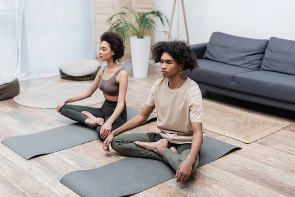 Africano Americano Hombre Meditando Cerca Borrosa Novia Yoga Mat Casa —  Fotos de Stock