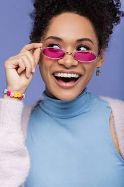 Mutlu Afro-Amerikalı kadın menekşe üzerinde izole edilmiş moda güneş gözlüklerini ayarlıyor. 