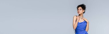 Kıvırcık, genç, Afro-Amerikalı, parlak mavi elbiseli kadın. Gri pankartta izole edilmiş.