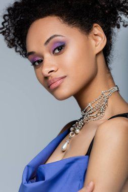 Kıvırcık Afro-Amerikan kadın leylak göz farı ile gri kameraya bakıyor.