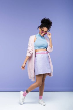 Dövmeli mutlu Afro-Amerikalı bir kadın. Mor üzerine son moda güneş gözlüğü takıyor.
