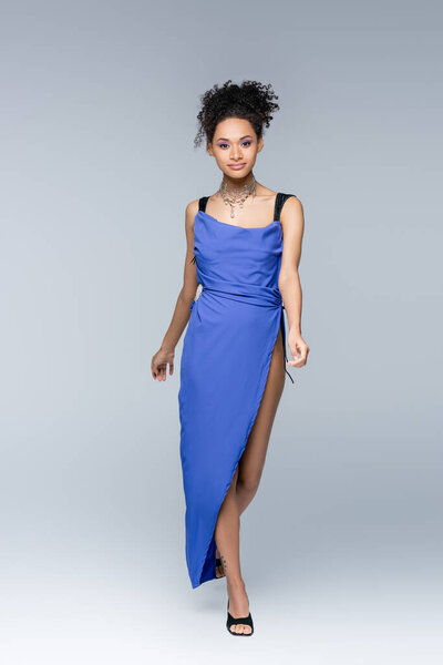Полная длина элегантный африканский американец женщина в ярко-синем платье ходить по серому