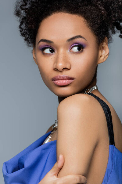 Curly african american woman with lilac eye shadow isolated on grey