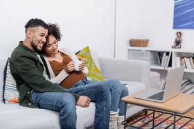 Pozitif Afro-Amerikan koca ve hamile kadın dizüstü bilgisayardan film izliyorlar.