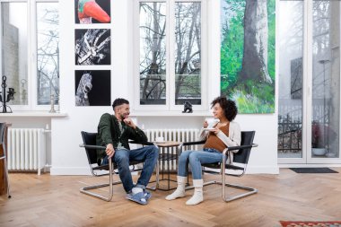 Neşeli Afrikalı Amerikalı adam elinde çay tutan hamile karısına bakıyor.