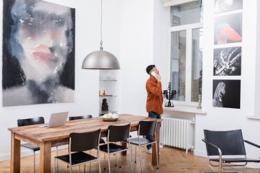 Afrikalı Amerikalı serbest çalışan akıllı telefondan konuşuyor ve modern apartmanın camına bakıyor.