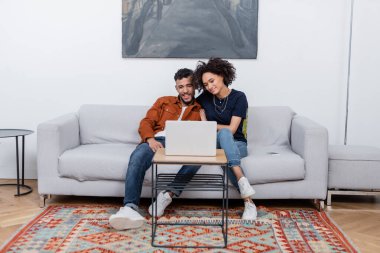 Modern dairede dizüstü bilgisayardan film izlerken gülümseyen genç Afrikalı Amerikalı çift.  