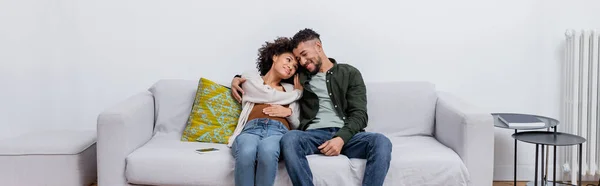 妊娠中のアフリカ系アメリカ人女性が幸せな夫と一緒に現代のアパートのソファに座って — ストック写真