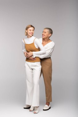 Neşeli orta yaşlı bir anne, mutlu kızını gri üzerinde kucaklıyor. 