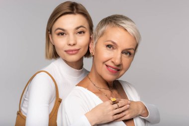Genç kız gülümseyen orta yaşlı anne ve gri renkli kameraya bakıyor.