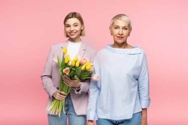 Orta yaşlı bir annenin yanında elinde bir buket lale tutan mutlu bir genç kız. Pembe üzerine izole edilmiş.