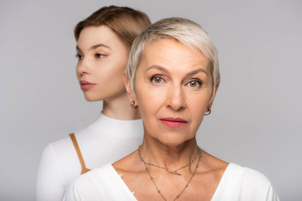 расплывчатая молодая женщина позади матери средних лет, изолированная от серого