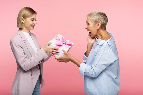 幸せな女性はピンクに隔離された興奮した成熟した母親にプレゼントをラップ与えます — ストック写真