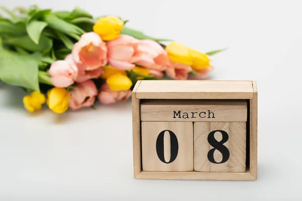 wooden calendar with 8 march lettering near blurred tulips on white