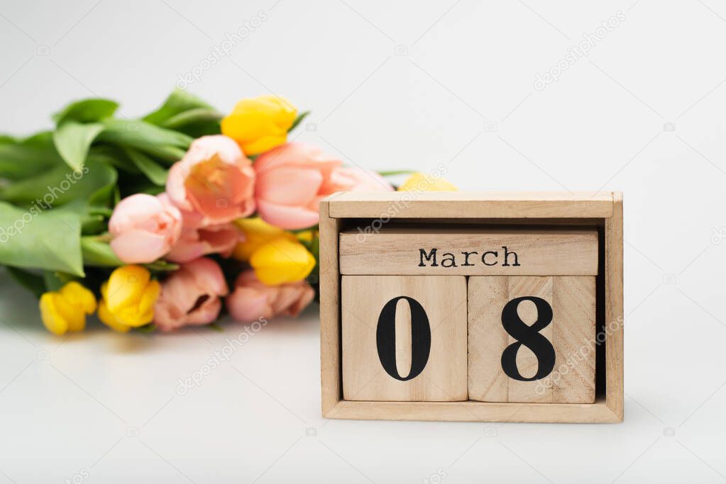wooden cubes with 8 march lettering near blurred tulips on white
