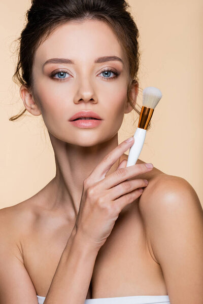 Pretty brunette model holding cosmetic brush while posing isolated on beige 