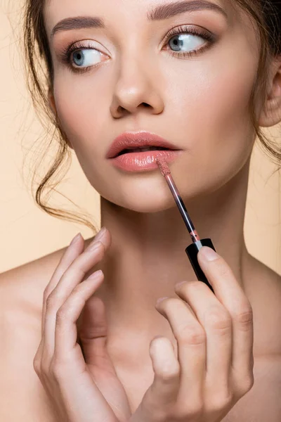 Portrait Pretty Woman Applying Lip Gloss Looking Away Isolated Beige — Stock Photo, Image