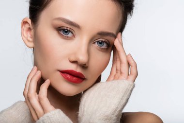 Yüze dokunan kırmızı dudaklı güzel bir model ve beyaza izole edilmiş kameraya bakıyor.