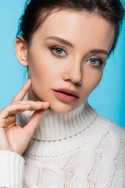 Örgü kazaklı bir model portresi mavi üzerine izole edilmiş kameraya bakıyor.