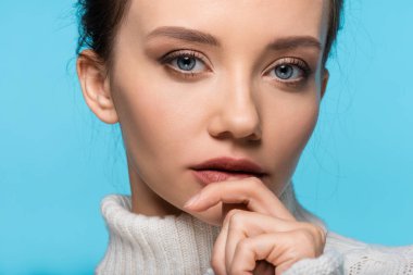 Mavi üzerine izole edilmiş ağzın yanında el ele tutuşan kazaklı güzel kadın portresi.