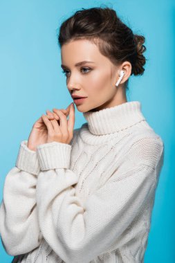 Mavi üzerine izole edilmiş kulaklık kullanan örgü kazaklı genç bir kadın.