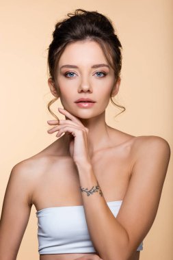 Beyazlı dövmeli kadın bej renkli kameraya bakıyor. 