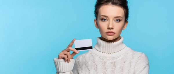 Молодая женщина в теплом свитере держит кредитную карту изолированы на синий, баннер 
