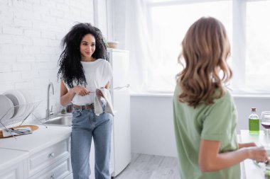 Memnun Afrikalı Amerikalı kadın mutfakta sarışın kız arkadaşına bakıyor.