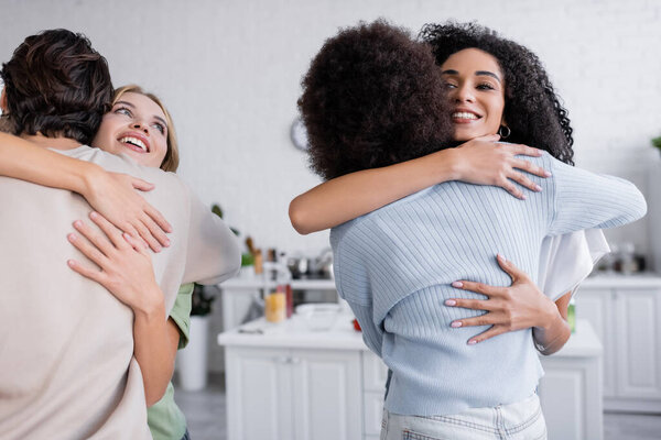 happy interracial friends hugging in modern apartment
