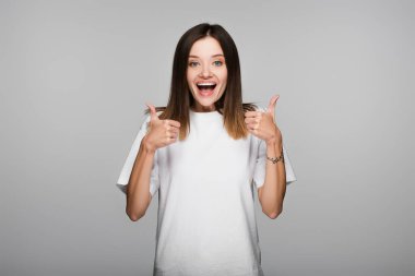 Gri renkli kameraya bakarken baş parmak gösteren çok mutlu bir kadın.