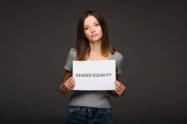 Genç esmer kadın, gri üzerine yazılı cinsiyet eşitliği yazılı bir pankart tutuyor.