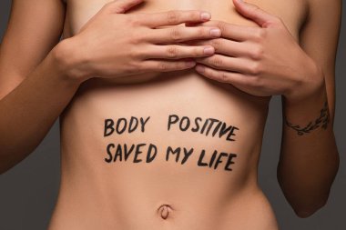 cropped view of nude woman with body positive saved my life inscription on body isolated on dark grey clipart