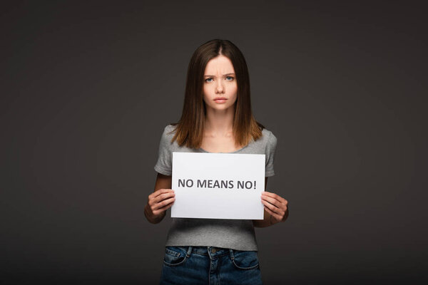 young and serious woman holding card with no means no lettering isolated on grey