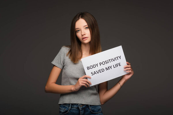 brunette woman holding paper with body positivity saved my life lettering isolated on grey