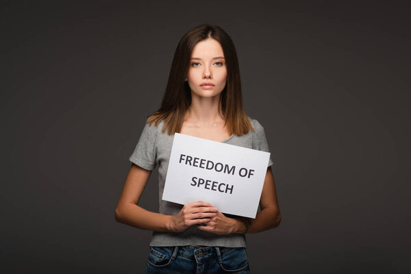 young brunette woman holding card with freedom of speech lettering isolated on grey