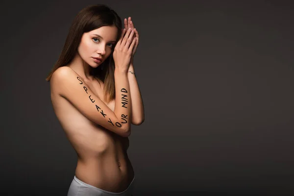 woman in panties, with speak your mind lettering on arm, looking at camera isolated on dark grey