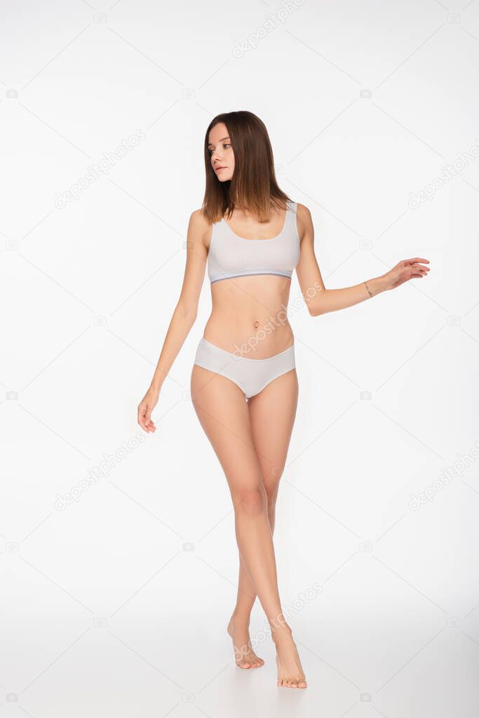 full length view of fit woman in underwear walking on tiptoes on white background