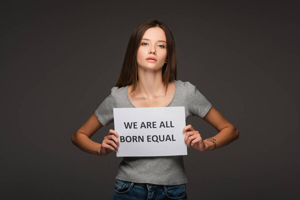 young brunette woman holding placard with we are all born equal lettering isolated on grey