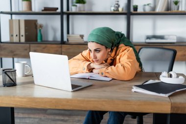 young muslim woman looking at laptop during webinar at home clipart
