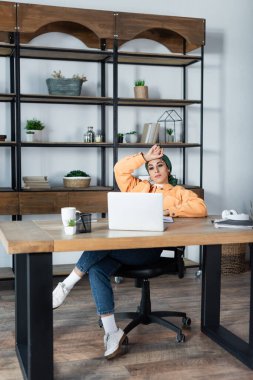Bilgisayardaki online seminer sırasında oturma odasında oturan Müslüman kadının tam boy görüntüsü.