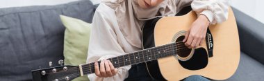 Evdeki kanepede akustik gitar çalan müslüman kadın görüntüsü, afiş.