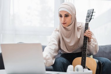Gitarlı Arap kadın evde bulanık dizüstü bilgisayara bakıyor.