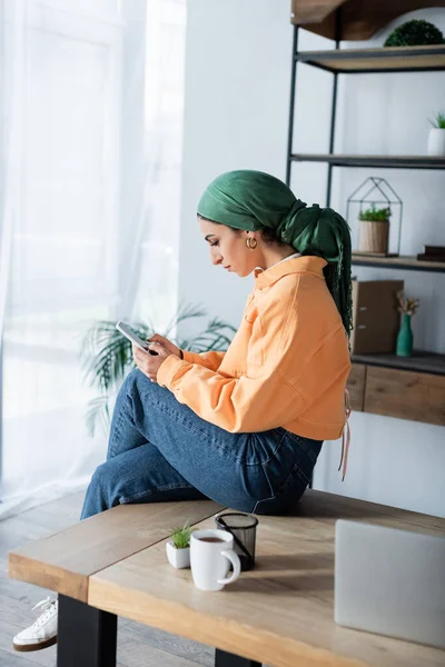 Junge Muslimische Studentin Taschentuch Sitzt Hause Schreibtisch Und Benutzt Handy — Stockfoto