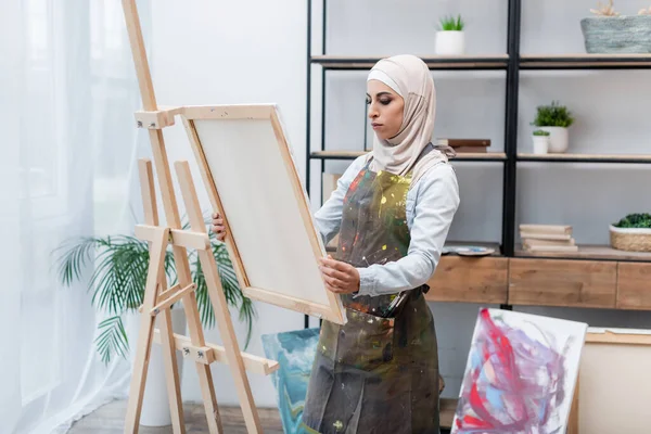 Muslimsk Kvinna Hijab Och Förkläde Håller Duk Nära Staffli Hemma — Stockfoto