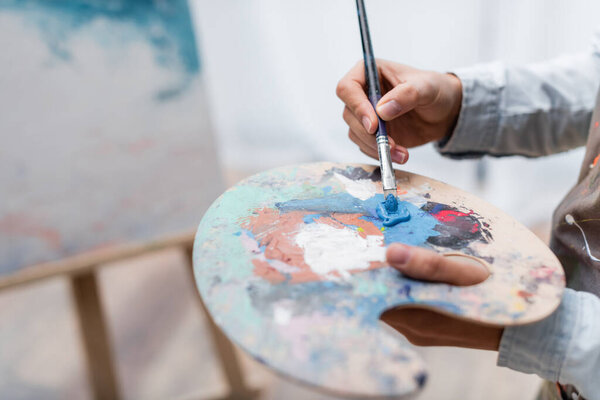 partial view of artist mixing oil paints on palette on blurred background