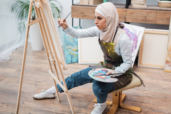 full length view of muslim woman drawing on easel at home