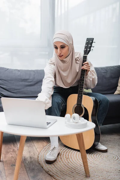 Joven Mujer Musulmana Sentada Cerca Computadora Portátil Sosteniendo Guitarra Acústica — Foto de Stock