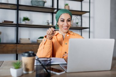 Evdeki online derste bilgisayarı gösteren neşeli Müslüman kadın.