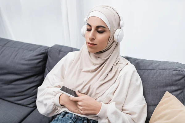 Arabská Žena Poslouchá Hudbu Sluchátkách Zatímco Sedí Gauči Zavřenýma Očima — Stock fotografie