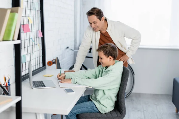 Smiling Father Standing Son Writing Notebook Devices Home — Stock Photo, Image